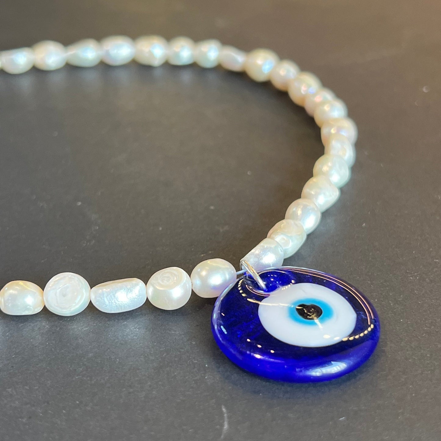 Pearl bracelet with a blue evil eye charm on a dark background