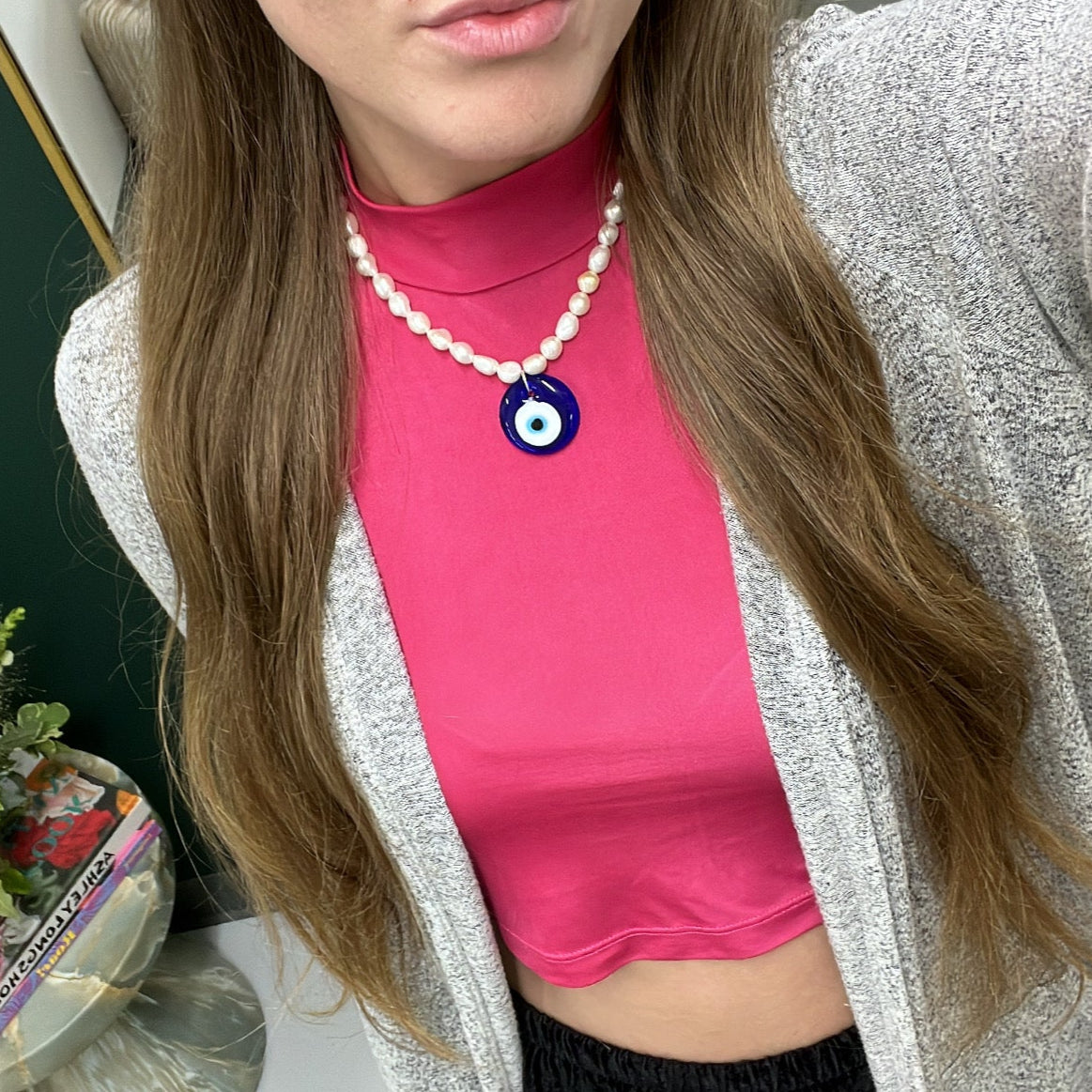 Person wearing a pink top with a blue eye design, sitting indoors with flowers in the background.