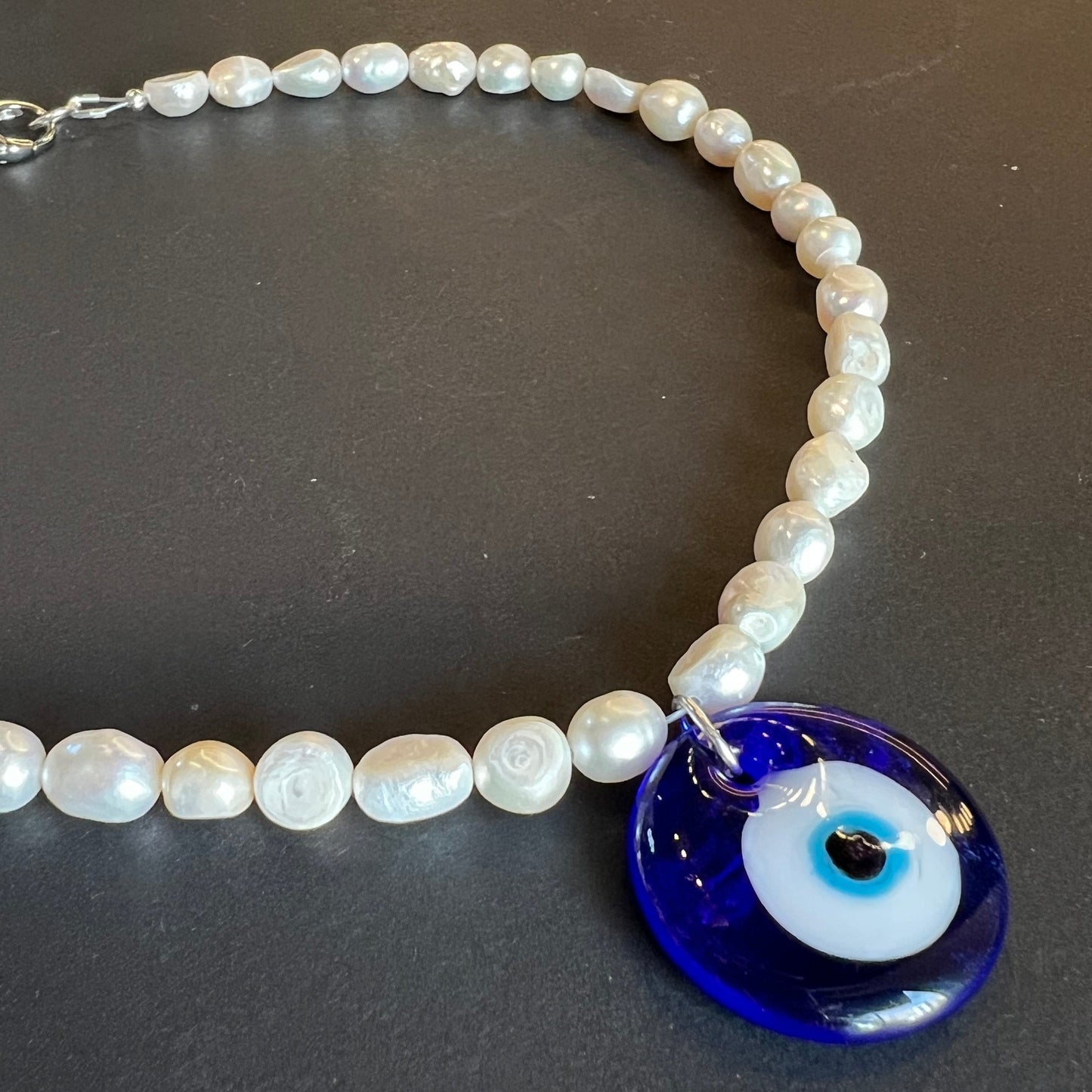 Pearl necklace with a blue evil eye charm on a dark background