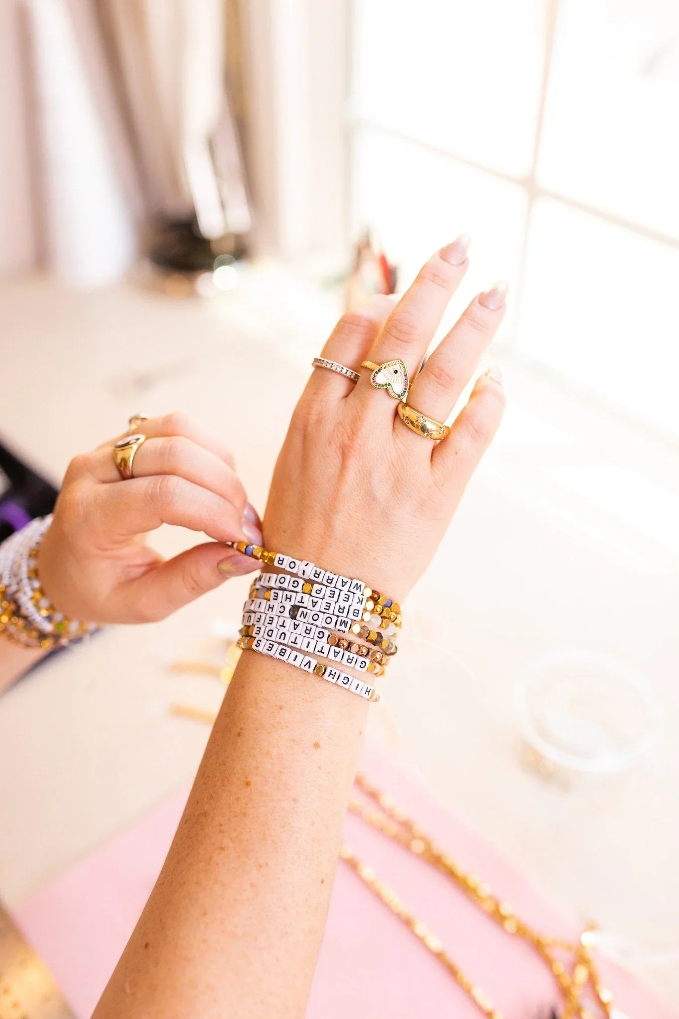 Assorted handcrafted beaded bracelets with pearls, gemstones, gold, silver, charms, and mantra beads displayed in a layered stack.