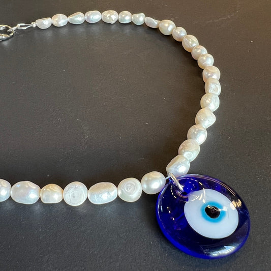 Pearl necklace with a blue evil eye charm on a dark background