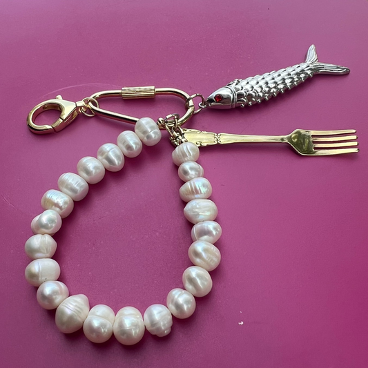 Pearl bracelet with a fish-shaped keychain and fork on a purple surface