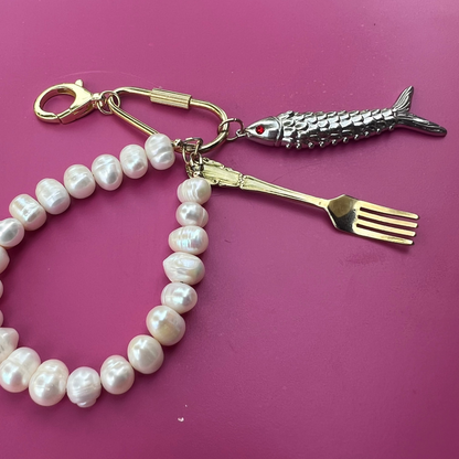Pearl keychain with fork and knife charms on a pink surface