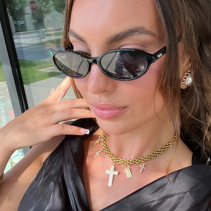 Woman wearing sunglasses and gold jewelry with a blurred outdoor background